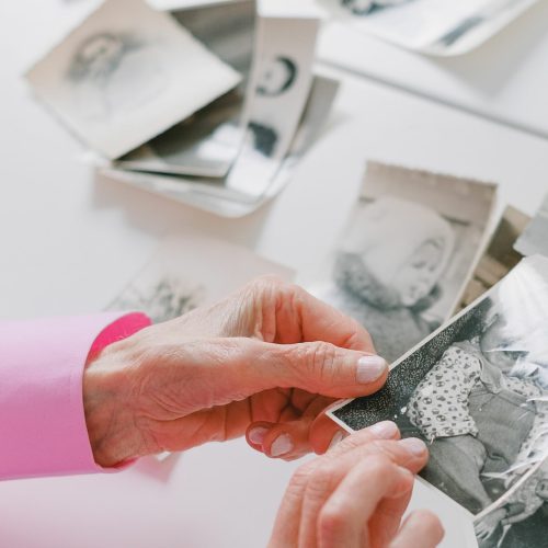 An elderly person with pink sleeves is reviewing nostalgic black and white photographs at a table.